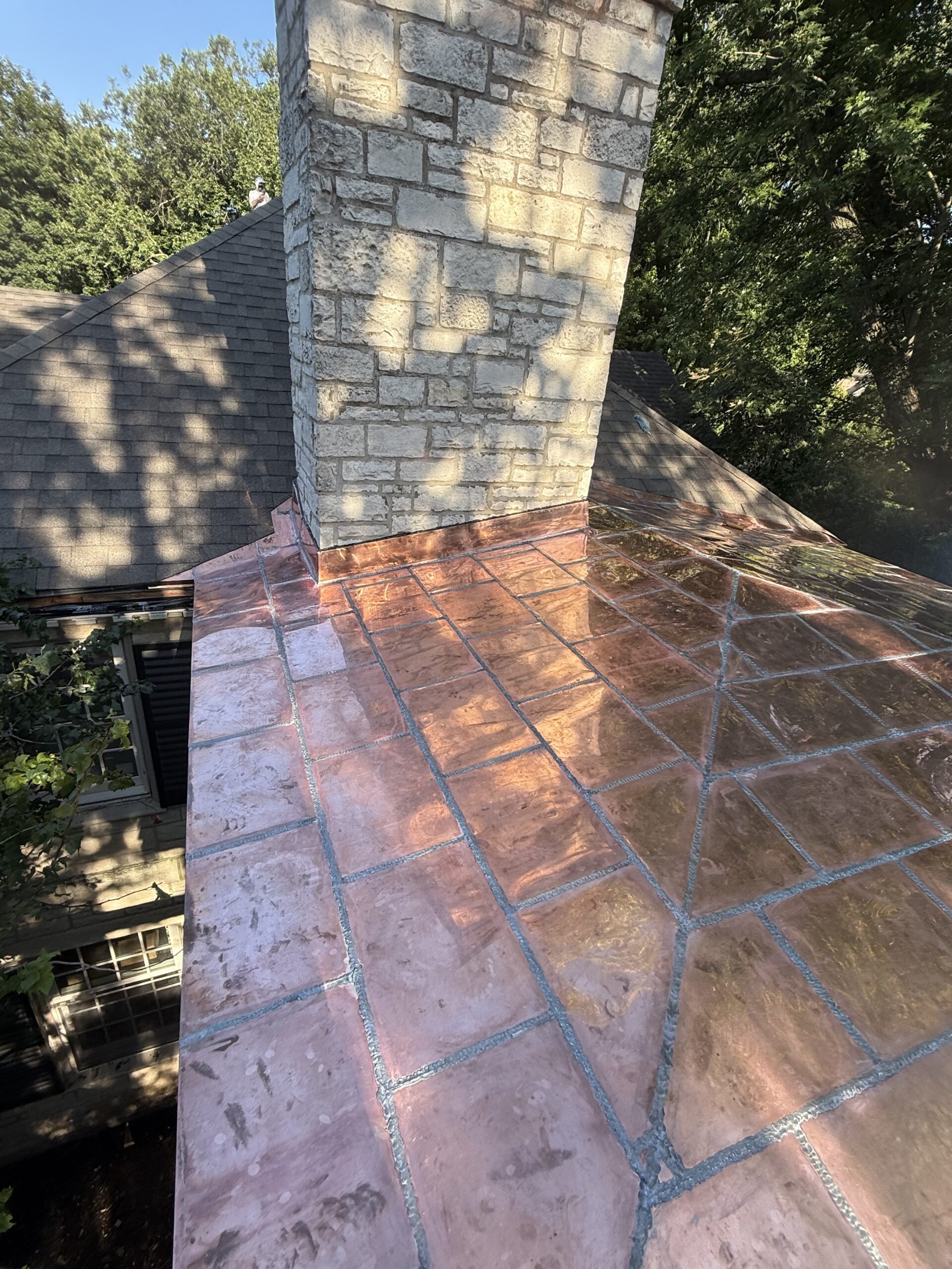 copper roof panels welded together with copper flashing around chimney
